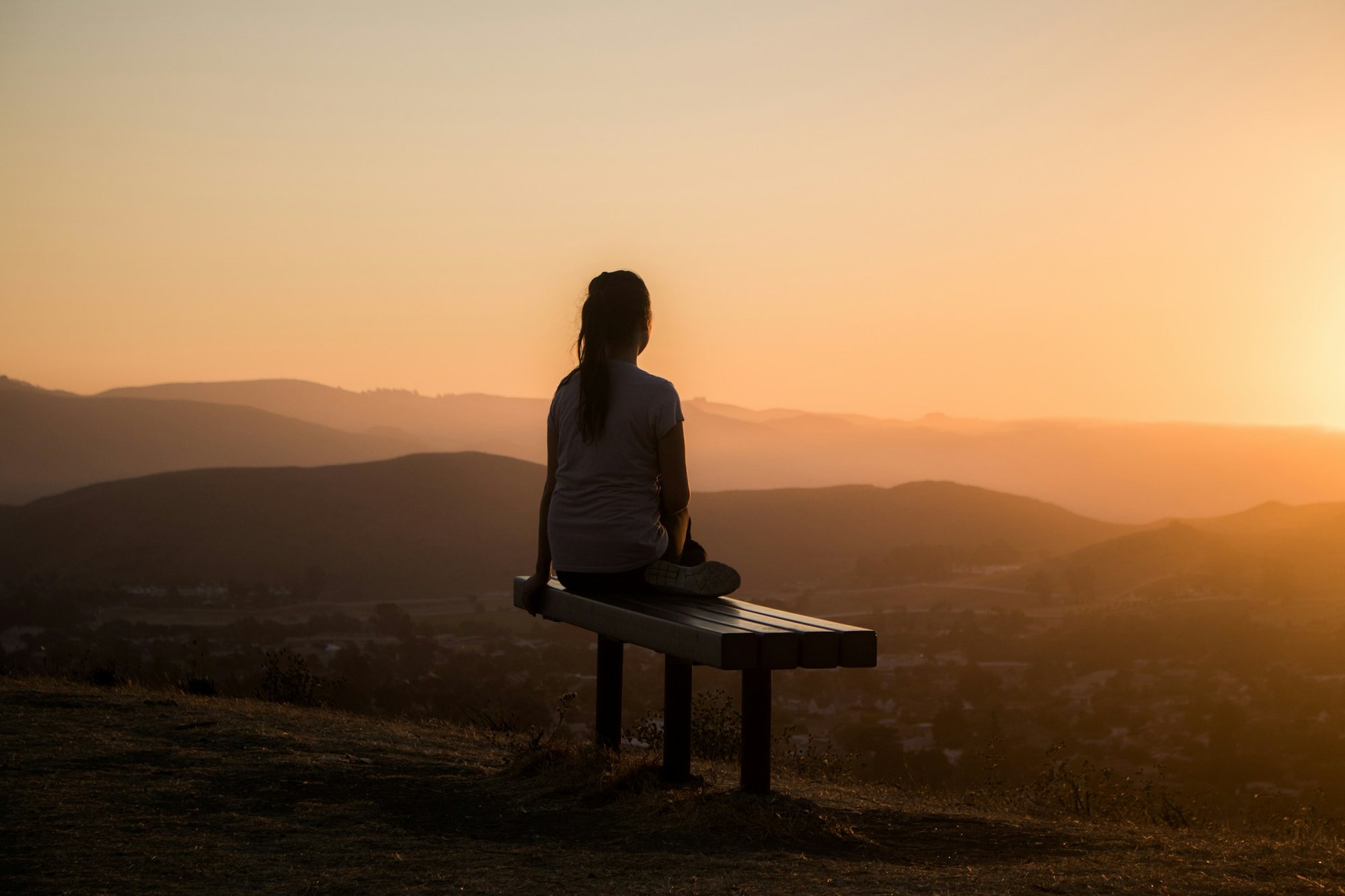 Silueta de una persona sentada frente al horizonte al atardecer