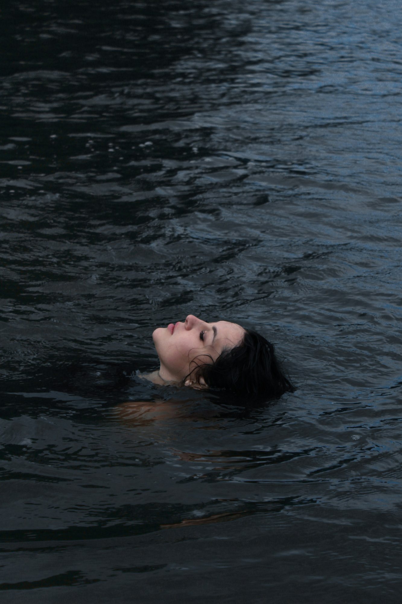 Mujer flotando en calma sobre agua oscura