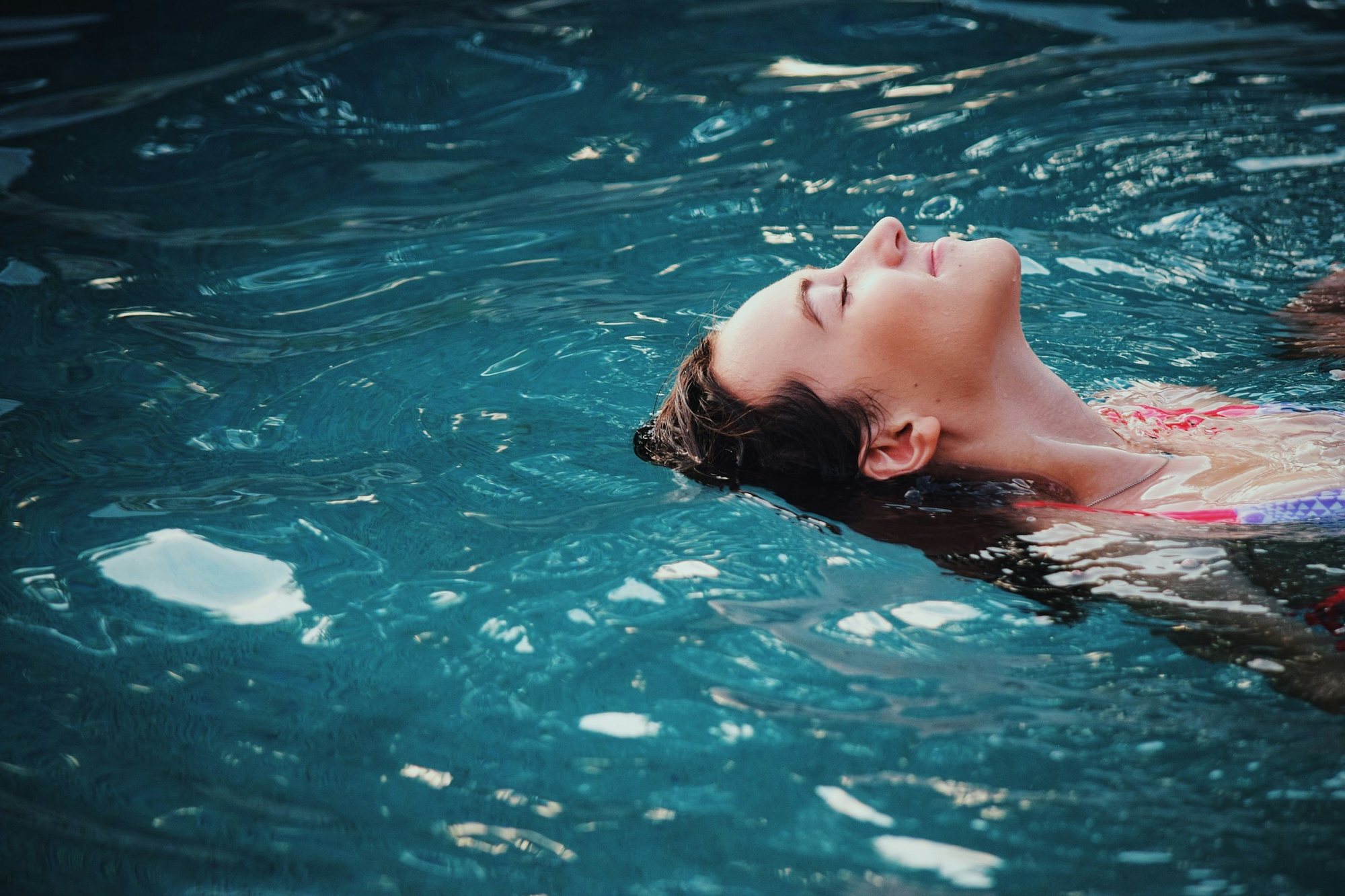 Mujer flotando de espaldas con los ojos cerrados en agua turquesa